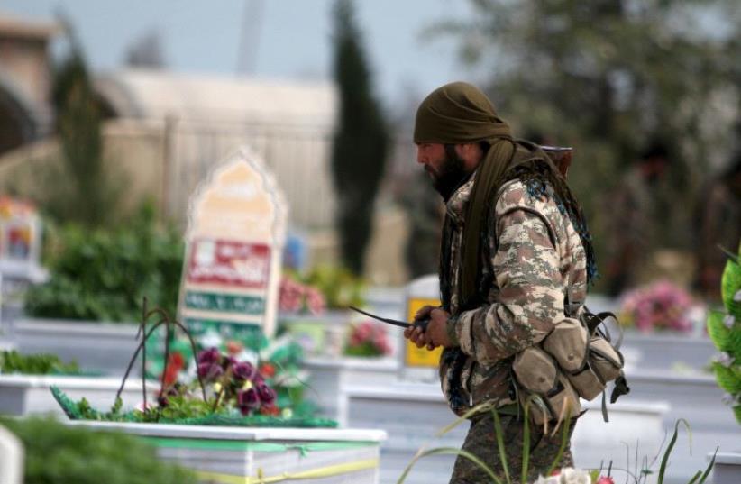 A Kurdish People's Protection Units (YPG) fighter walks near graves of fellow fighters during a visit to a YPG graveyard in Qamishli, Syria (photo credit: RODI SAID / REUTERS)