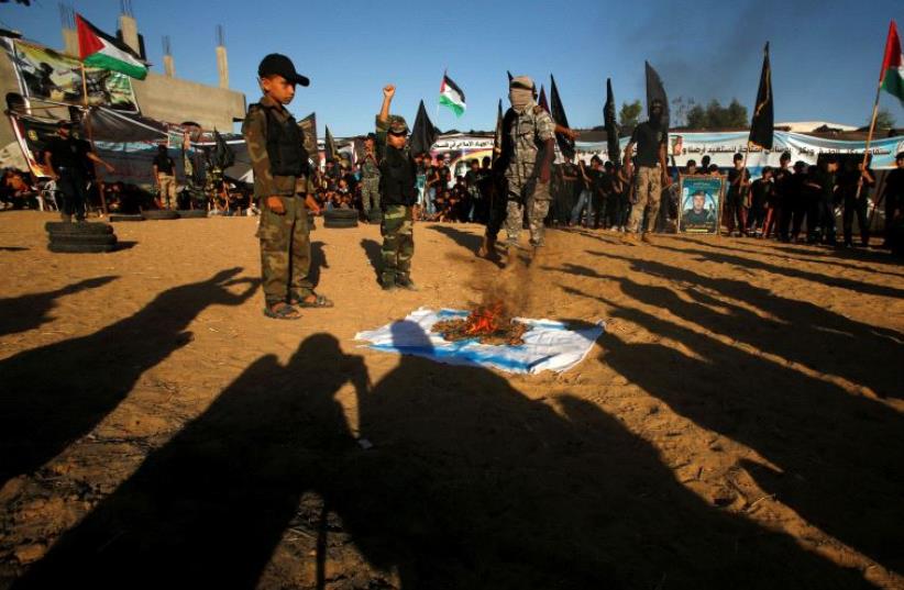 Palestinians burn an Israeli flag during a military-style graduation ceremony at a summer camp organized by the Islamic Jihad Movement in Khan Younis in the southern Gaza Strip (photo credit: SUHAIB SALEM / REUTERS)