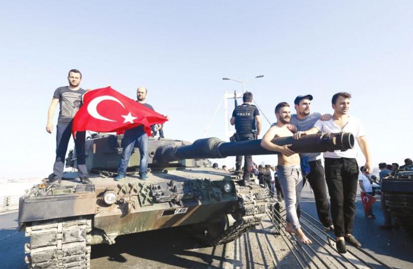 People pose near a tank after troops involved in the coup surrendered on the Bosporus Bridge in Istanbul on July 16 (photo credit: REUTERS)