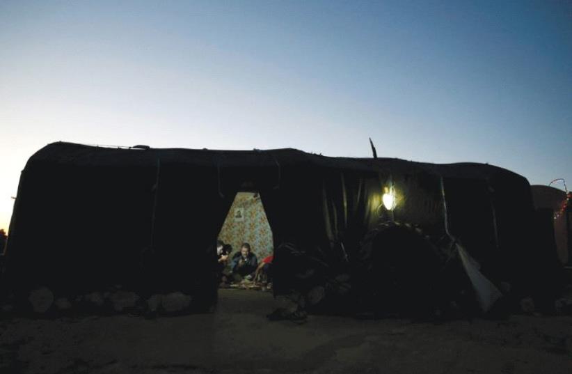 A Beduin man eats with his family in their tent in Sussiya near Hebron (photo credit: AMMAR AWAD/REUTERS)