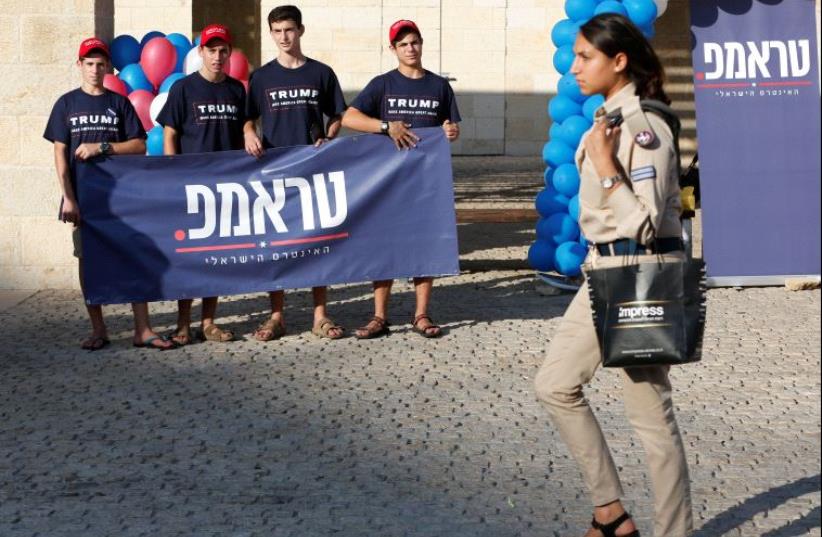 An Israeli soldier walks past members of the US Republican party's election campaign team in Israel, who are holding a banner in support of Republican US presidential nominee Donald Trump, during a campaign aimed at potential American voters living in Israel, near a mall in Modi'in, Israel. (photo credit: REUTERS)