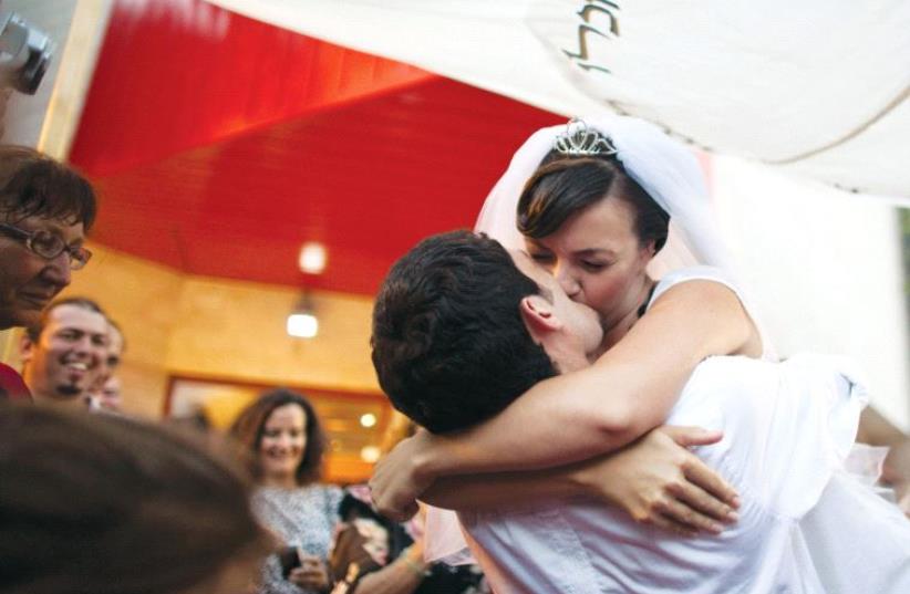 A bride and groom kiss under the chuppah at their wedding (photo credit: NIR ELIAS / REUTERS)
