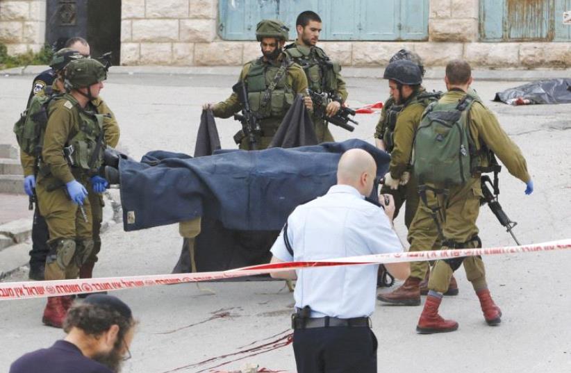 KFIR BRIGADE fighters carry the body of one of two terrorists killed after they attacked a soldier in the Tel Rumeida neighborhood of Hebron on March 24. (photo credit: REUTERS)