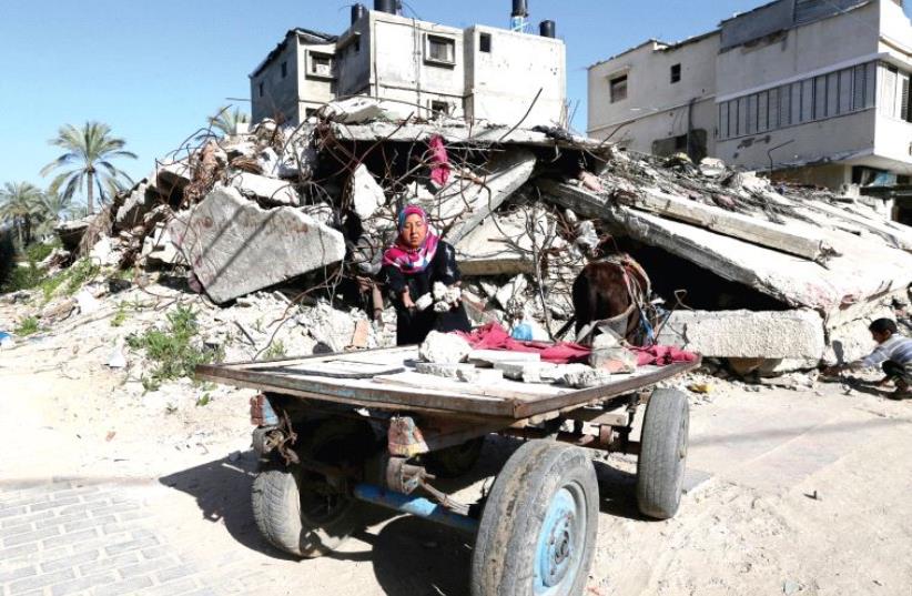 A Palestinian woman collects bricks from a house destroyed during the 2014 Gaza war (photo credit: REUTERS)