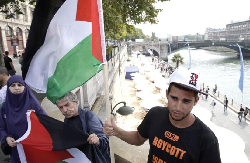 A man wearing a T-shirt of the BDS movement holds a Palestinian flag during a protest against the ‘Tel-Aviv sur Seine’ beach attraction in central Paris last summer (photo credit: AFP PHOTO)