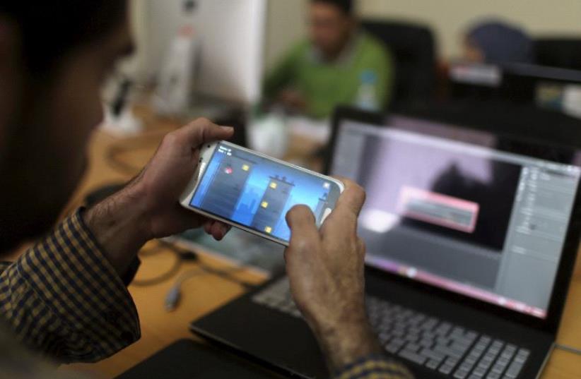 A young Palestinian entrepreneur displays on his mobile a game that he developed at Gaza Sky Geeks office, in Gaza City January 18, 2016. (photo credit: REUTERS)