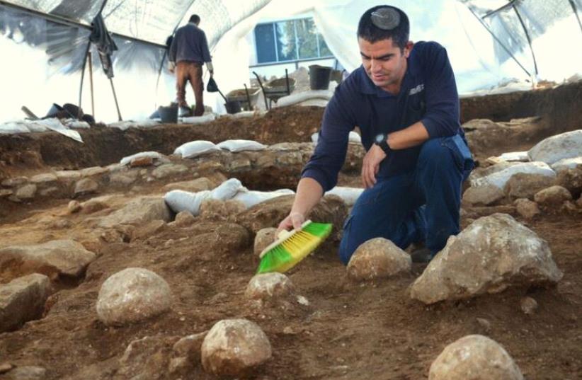  IAA Excavation Co-Director Kfir Arbib cleans one of the unearthed sling stones found at the site (photo credit: YOLI SHWARTZ AND ISRAEL ANTIQUITIES AUTHORITY)