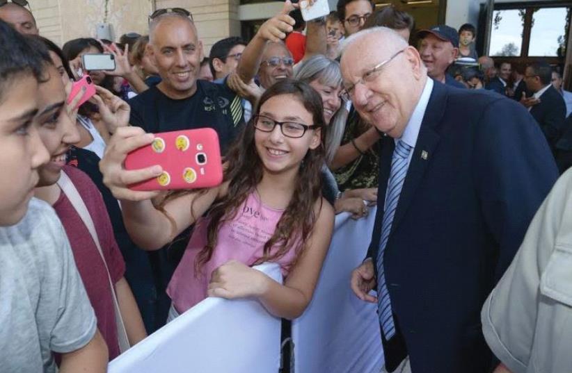 PRESIDENT REUVEN RIVLIN poses with a guest for a selfie. At right, guests photograph and reach out to shake hands with him. (photo credit: ROY BERKOVICH)