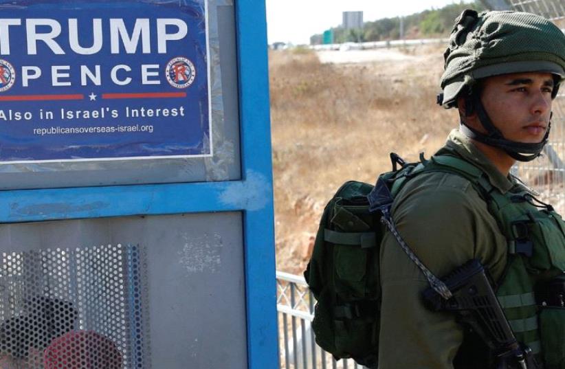 A soldier stands next to a bus stop with a pro-Trump poster near the West Bank Jewish settlement of Ariel (photo credit: REUTERS)