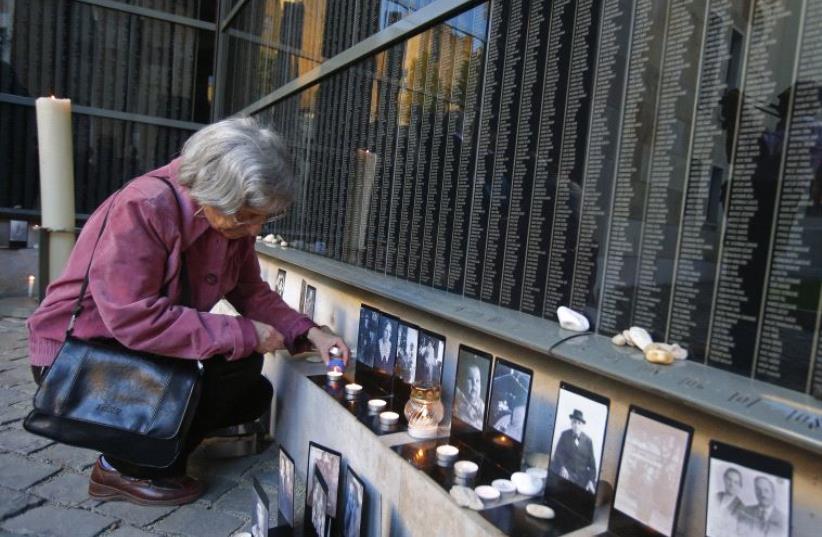 A woman lights a candle in front of a wall containing the names of victims, during the Holocaust memorial day at Budapest's Holocaust Memorial Centre April 16, 2013 (photo credit: REUTERS)