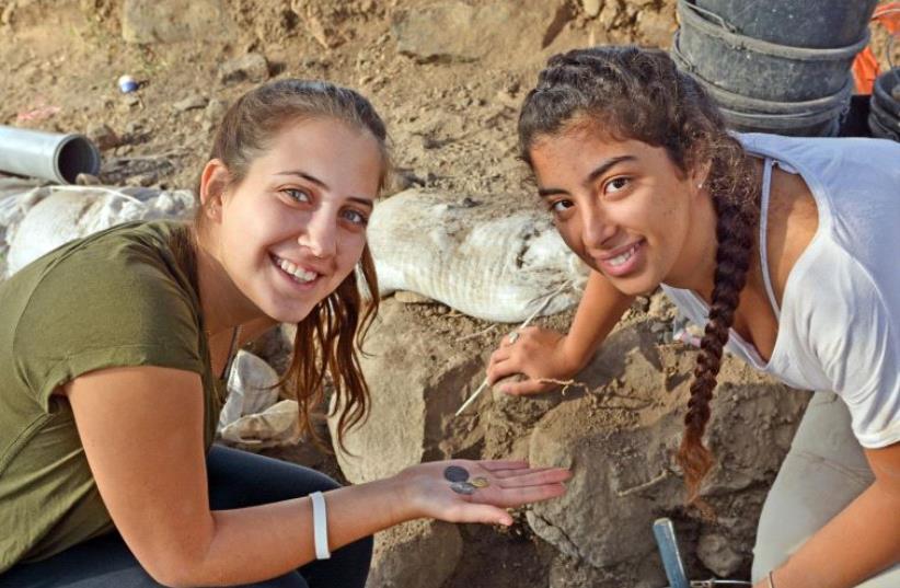 Dor Yogev and Ella Dicks hold coins discovered in the town of Kama (photo credit: GILAD CHINMON / ISRAEL ANTIQUITIES AUTHORITY)