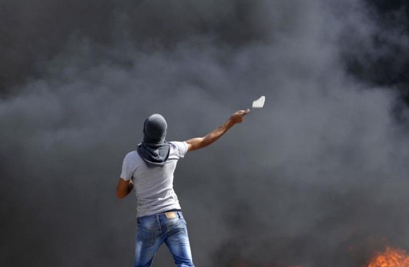 A Palestinian throws a stone towards Israeli troops during clashes at Qalandia checkpoint (photo credit: REUTERS)