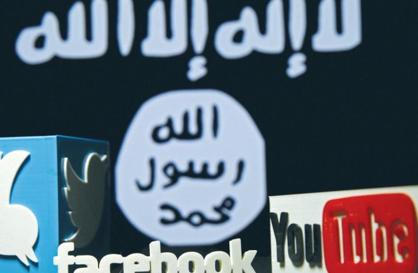 A 3-D PLASTIC representation of the Twitter, Facebook and YouTube logos is displayed in front an Isis flag. Islamic State is considered a pioneer among terrorist organizations regarding innovation in the cyber world. (photo credit: DADO RUVIC/REUTERS)