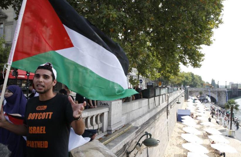 A man wearng a T-shirt with the message, "Boycott Israel Apartheid" holds a Palestinian flag during a protest. (photo credit: REUTERS)