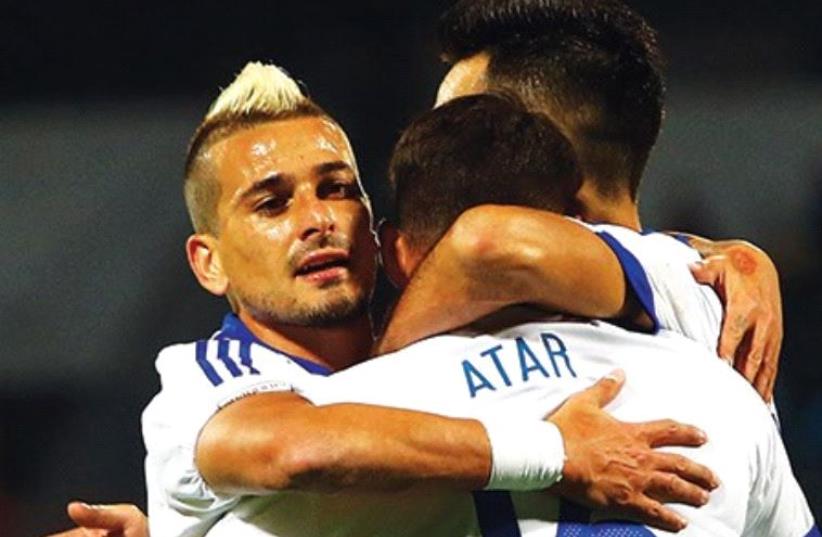 Israel national team midfielders Maor Buzaglo (left) and Eran Zahavi embrace striker Eliran Atar (center) after he scored the side’s third goal in the 3-0 win over Albania on Saturday. (photo credit: UDI ZITIAT)