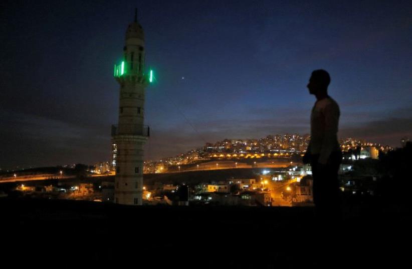 A man stands near a mosque opposite to a neighborhood in east Jerusalem November 13, 2016. (photo credit: REUTERS)