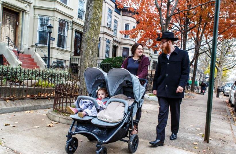 Chabad-Lubavitch Rabbi Mendel Alperowitz, right, Mussie Alperowitz, left, and their two daughters, ages 18 months and 2 months, walk in Crown Heights, Brooklyn. (photo credit: ELIYAHU PARYPA / CHABAD.ORG)