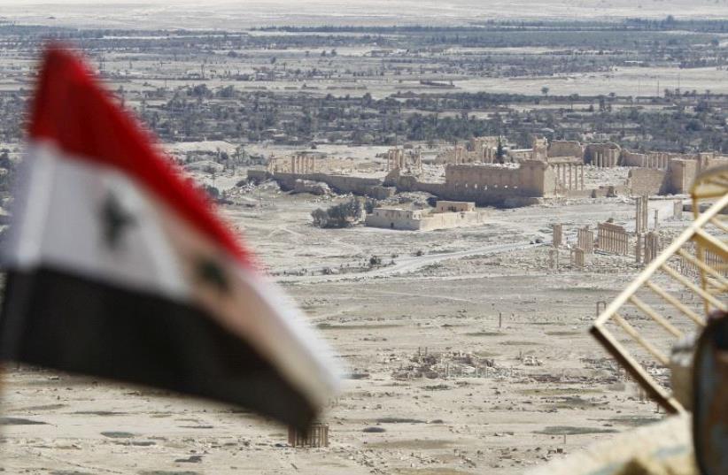  A Syrian national flag flutters as the ruins of the historic city of Palmyra are seen in the background, in Homs Governorate, Syria April 1, 2016. (photo credit: REUTERS)
