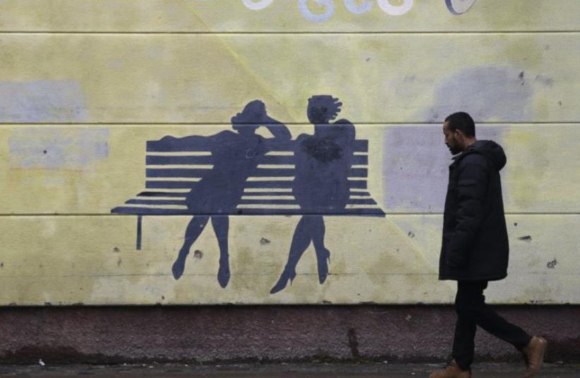 A man walks past a mural in the Husby suburb of Stockholm. In Husby, the roads still bear charred marks from cars torched in Sweden's worst riots for years, underscoring the Nordic state's struggle to integrate a record number of immigrants and challenging its open door traditions.  (photo credit: REUTERS)