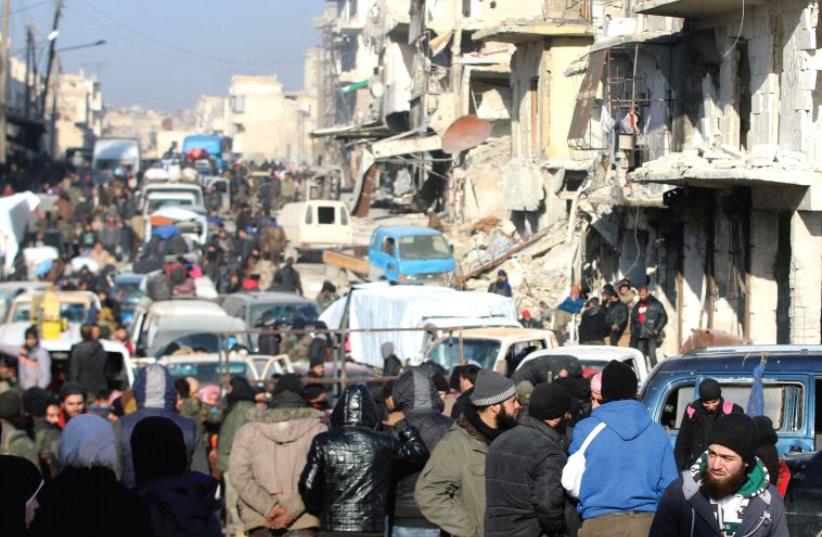 SYRIAN REBELS and civilians wait near damaged buildings to be evacuated from a rebel-held sector of eastern Aleppo. (photo credit: REUTERS)