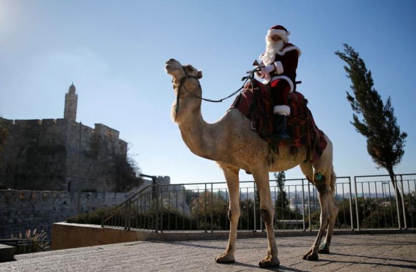 Israeli-Arab Issa Kassissieh wears a Santa Claus costume as he rides a camel during an annual Christmas tree distribution by the Jerusalem municipality, in Jerusalem's Old City December 20, 2016 (photo credit: REUTERS)