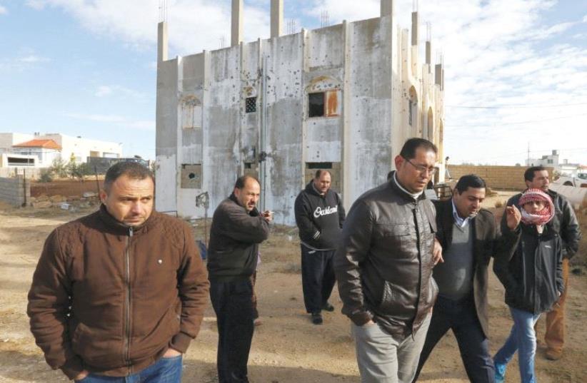 PEOPLE WALK past a building that was the site of clashes between Jordanian police and Islamist gunmen in the village of Garifla, in Karak, yesterday. (photo credit: MUHAMMAD HAMED / REUTERS)
