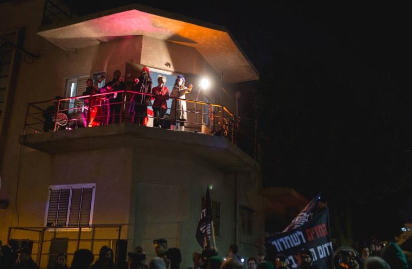 Anti-immigrant protestors wave flags as Christmas carolers sing from a balcony in the Neve Sha'anan neighborhood on Thursday ​​ (photo credit: OMER BITAS)