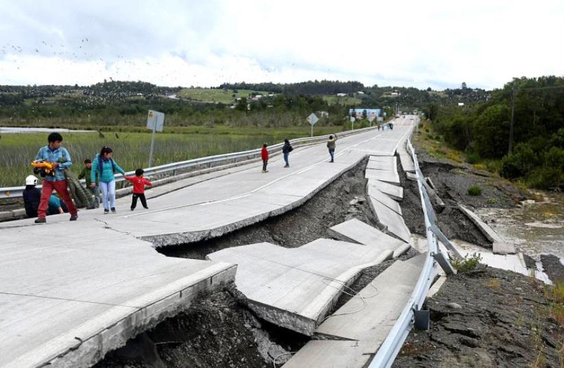 People inspect damage caused on highway 5 south on Chiloe Island off the Pacific coast of southern Chile, by a 7.7-magnitude earthquake on December 25, 2016 (photo credit: ALVARO SANTA ANA/ATON CHILE/AFP)