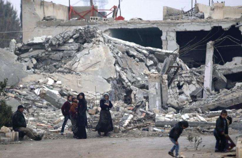 People stand near near rubble of damaged buildings in the northern Aleppo countryside in Syria in December 2016 (photo credit: REUTERS)