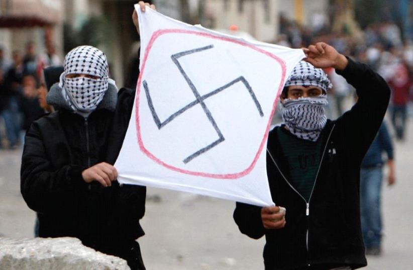 PALESTINIANS HOLD a sign depicting a swastika during clashes at Kalandiya checkpoint on the road to Jerusalem in 2010.  (photo credit: REUTERS)