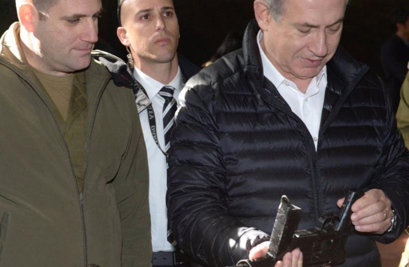 Prime Minister Benjamin Netanyahu examines a firearm during a visit to the West Bank (photo credit: AMOS BEN GERSHOM, GPO)