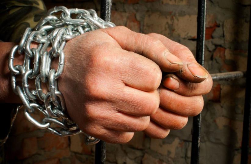 Man with hands tied up with chains behind the bars (illustrative) (photo credit: INGIMAGE)