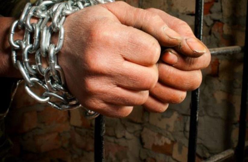 Man with hands tied up with chains behind the bars (illustrative) (photo credit: INGIMAGE)