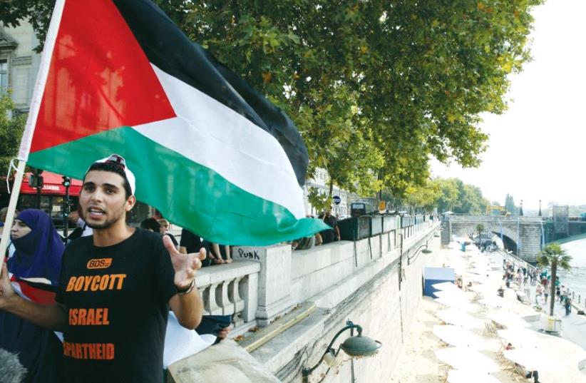 A man wearing a T-shirt with the message ‘Boycott Israel Apartheid’ holds a Palestinian flag during a protest event, in Paris in 2015 (photo credit: REUTERS)