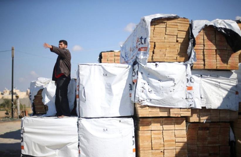 A Palestinian man gestures as he stands atop lumber brought in via Egypt, in Rafah in the southern Gaza Strip.  (photo credit: REUTERS)