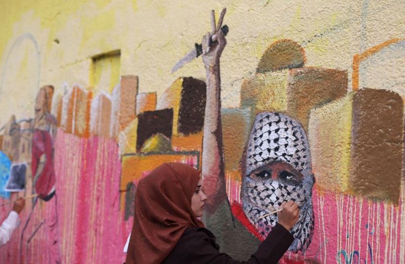 A Palestinian woman paints a mural, depicting a masked Palestinian holding a knife, in support of Palestinians committing stabbing attacks against Israelis, in Rafah in the southern Gaza Strip (photo credit: REUTERS)