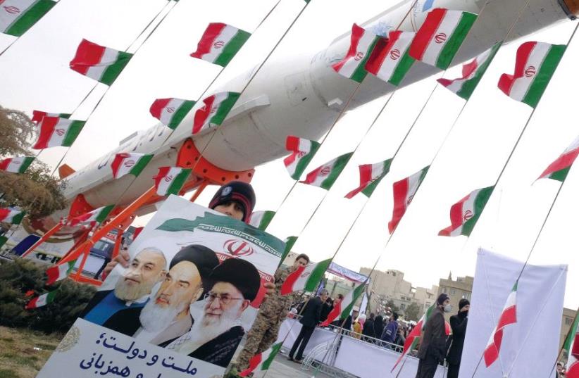 A boy holding a placard with pictures of (left to right) Iranian President Hassan Rouhani, the late founder of the Islamic Revolution Ayatollah Ruhollah Khomeini, and Iran’s Supreme Leader Ayatollah Ali Khamenei, poses in front of a model of a satellite-carrier rocket last year (photo credit: REUTERS)