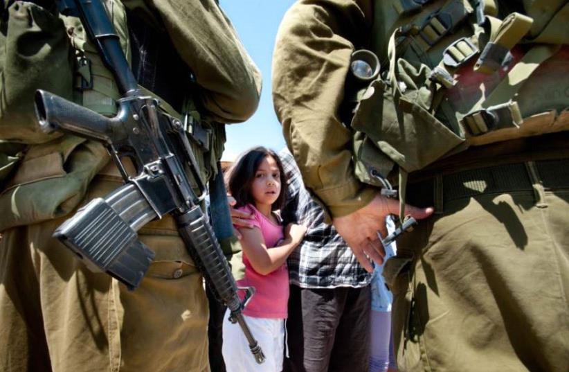Israeli soldiers next to a Palestinian girl as displayed in the report. (photo credit: WATCHLIST ON CHILDREN AND ARMED CONFLICT)