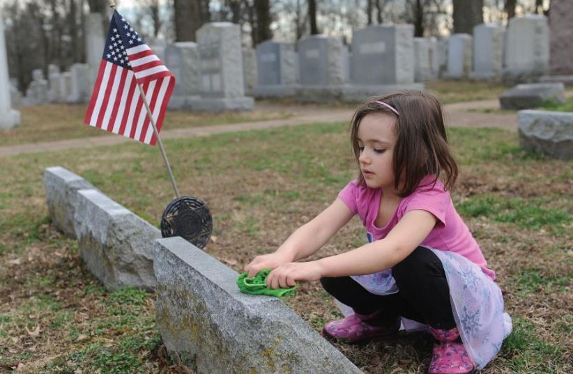 A child washes a headstone during a clean-up effort at the vandalized Chesed Shel Emeth Cemetery near St. Louis, Missouri, last February (photo credit: MICHAEL THOMAS / AFP)