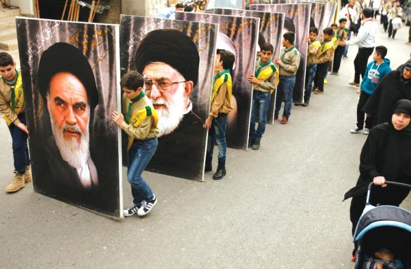 Hezbollah supporters carry portraits of the founder of Iran’s Islamic Republic, Ayatollah Ruhollah Khomeini (left), and supreme leader Ayatollah Ali Khamenei, as they march in the southern Lebanese town of Kfar Hatta on March 18 (photo credit: AFP PHOTO)