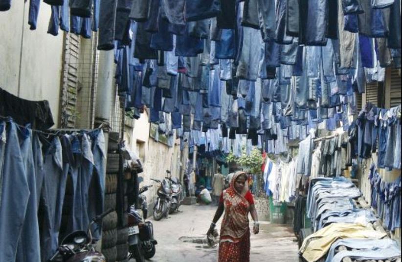 A woman walks through an alley where used pairs of jeans are hung to dry before they are sold in a secondhand clothes market in Kolkata, India, 2015 (photo credit: REUTERS)