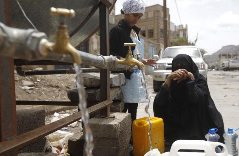 A woman fills jerrycans with clean water from a donated source amid a shortage of water supplies, in Yemen's capital Sanaa, April 14, 2016.  (photo credit: REUTERS)