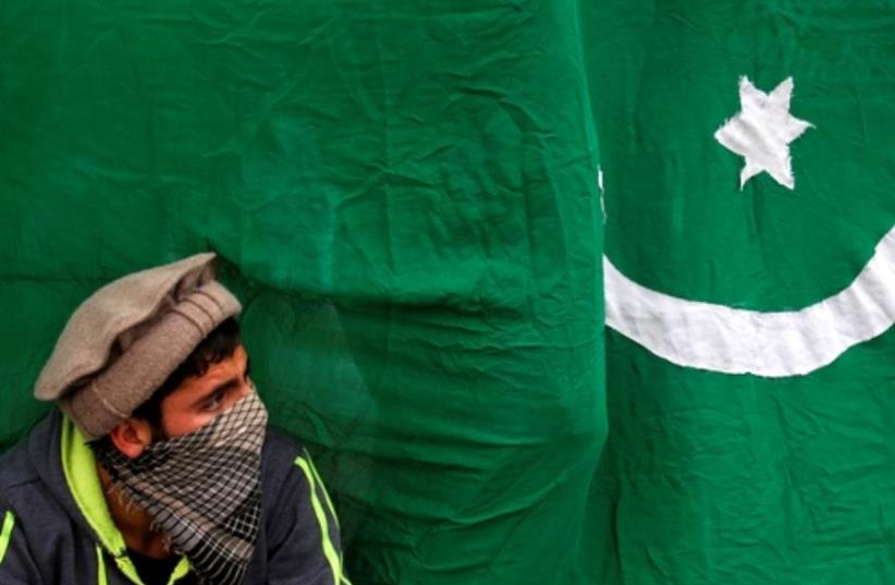 A masked protester sits next to a flag of Pakistan during an anti-Indian protest  (photo credit: REUTERS)