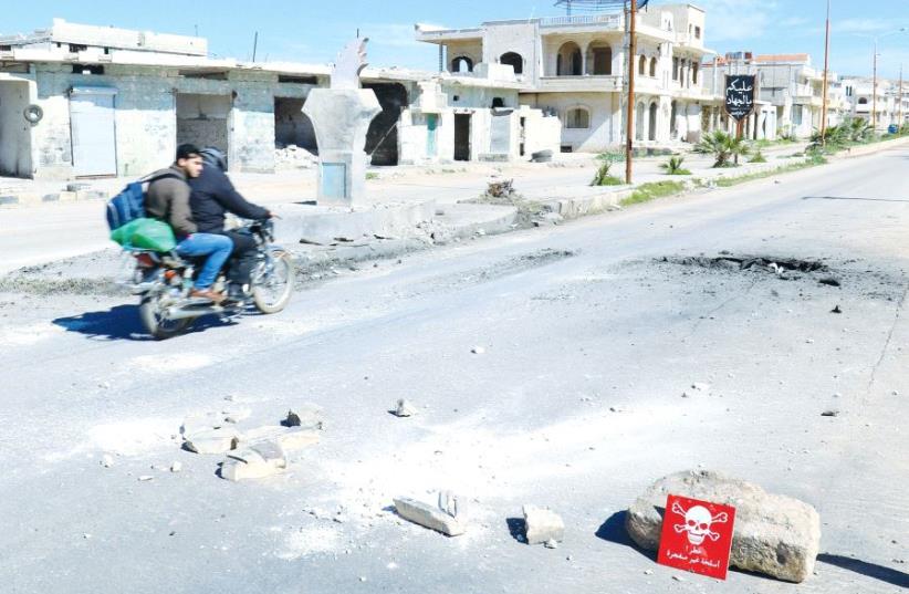 MEN RIDE a motorcycle yesterday past a hazard sign in rebel-held Khan Sheikhoun in Syria’s Idlib province near a site that was hit by an air strike on Tuesday (photo credit: REUTERS)