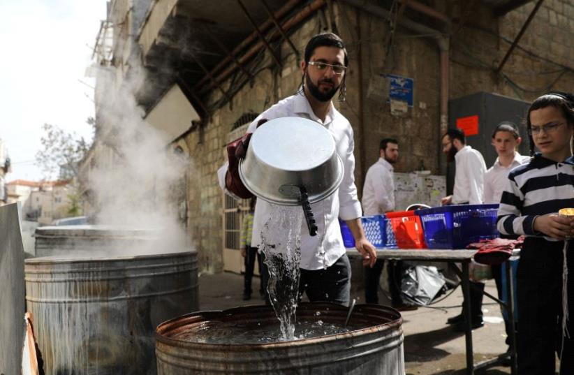 Ultra-Orthodox Jewish men sort their cooking utensils at they dip them in boiling water to remove remains of leaven in preparation for the Jewish holiday of Passover, in Jerusalem's Mea Shearim neighbourhood April 9, 2017 (photo credit: REUTERS)