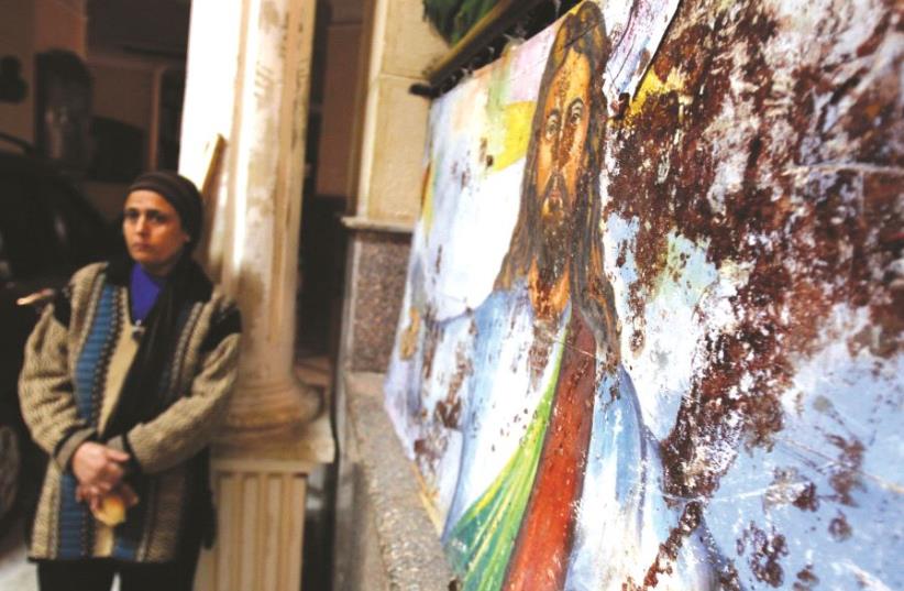Une femme près d'une peinture du Christ, tâchée de sang lors d'un attentat dans une église copte (photo credit: REUTERS)