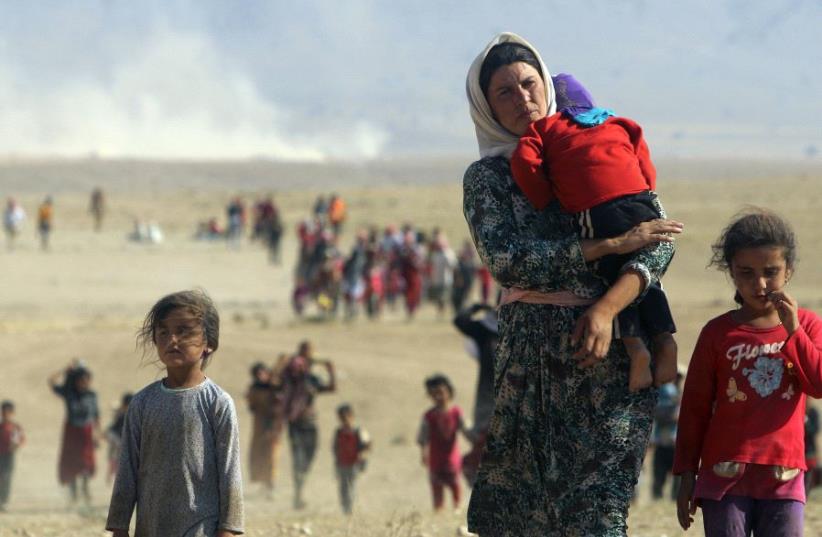 Displaced people from the minority Yazidi sect, fleeing violence from forces loyal to the Islamic State in Sinjar town, walk towards the Syrian border on the outskirts of Sinjar mountain near the Syrian border town of Elierbeh of Al-Hasakah Governorate in 2014 (photo credit: REUTERS)