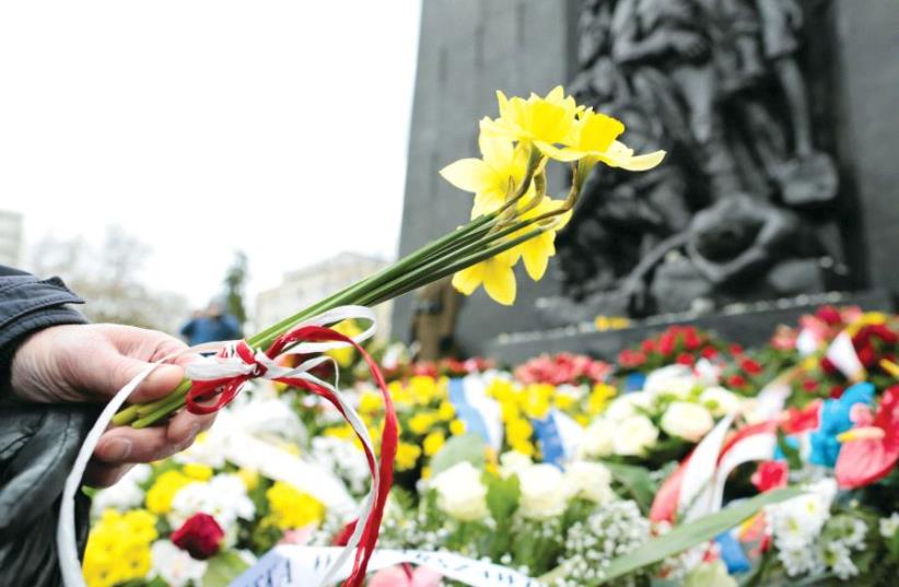 A man lays daffodils near the Ghetto Heroes monument in Warsaw (photo credit: REUTERS)