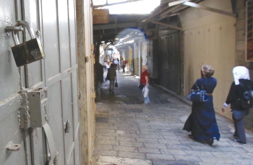 PEOPLE WALK past one of the more than 1,400 closed shops in the Muslim Quarter in the Old City of Jerusalem on April 27, 2017 (photo credit: MARC ISRAEL SELLEM/THE JERUSALEM POST)