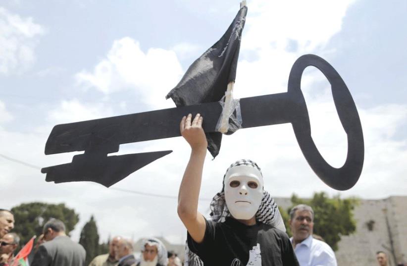 A Palestinian wearing a mask holds a cut-out of a key during a rally ahead of the ‘Nakba Day’ in Bethlehem in 2015 (photo credit: REUTERS)